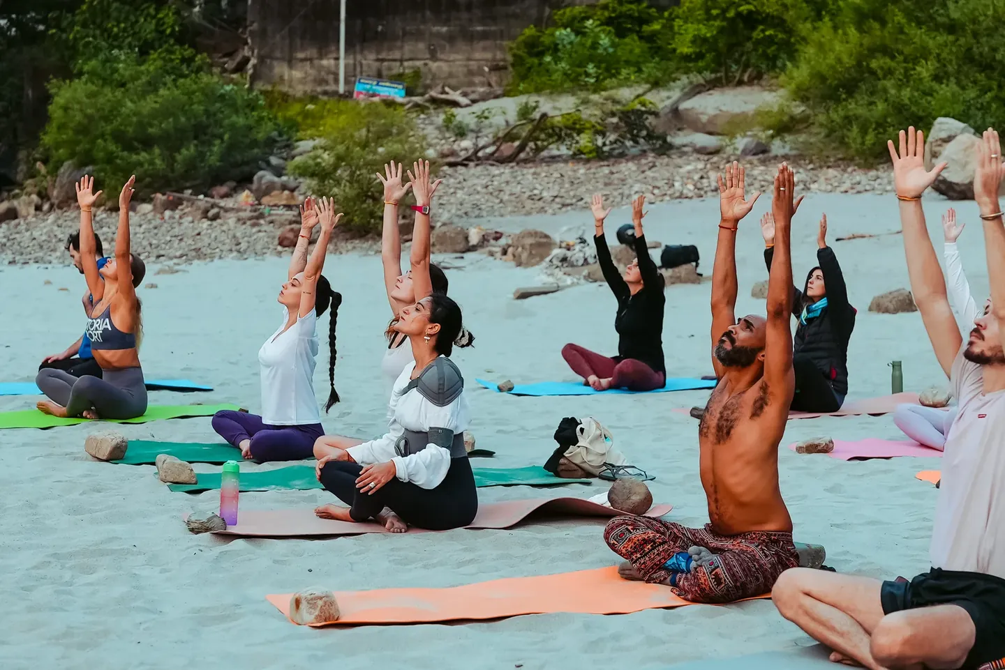 Participants raising their arms during seated yoga on the riverbank