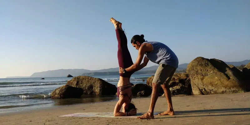 Teacher supporting a student in a beach headstand